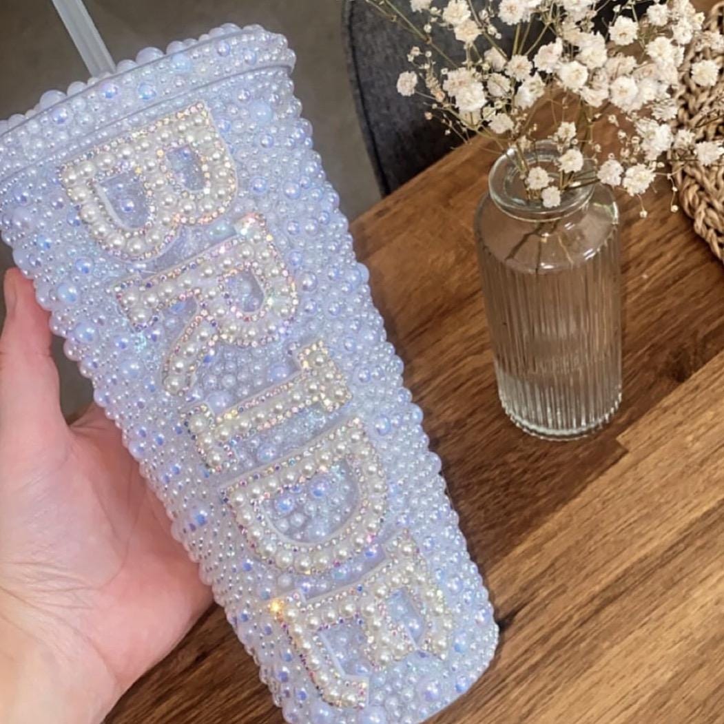 Blinged-out tumbler with 'Bride' on a wooden surface with flowers in the background