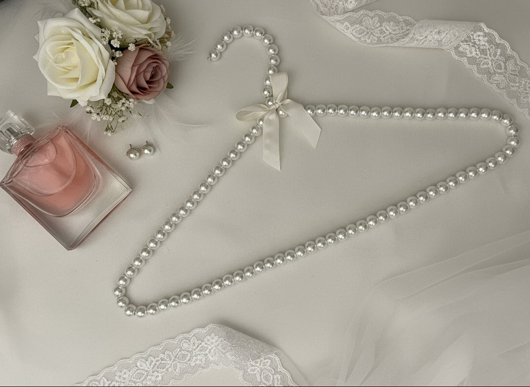 Pearl necklace on a fluffy white surface with a decorative flower and perfume bottle.